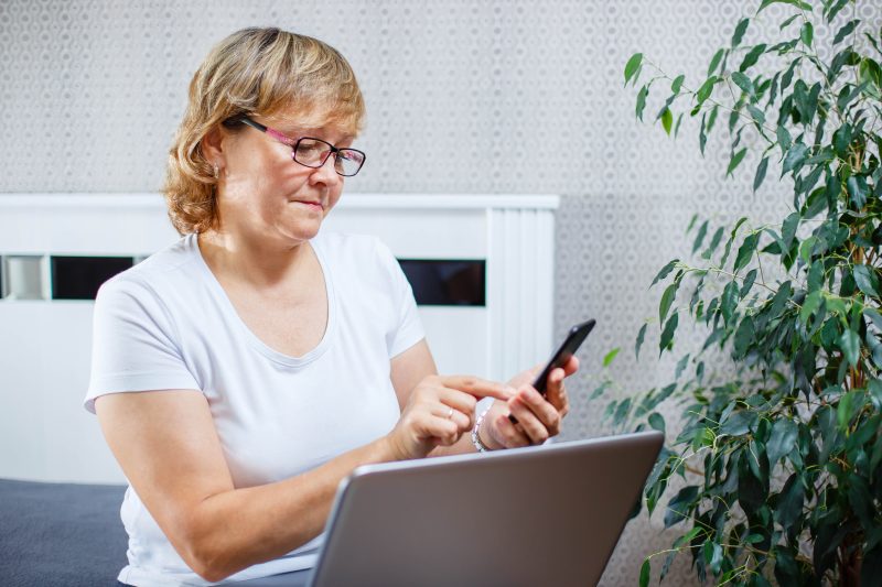 A woman using a smartphone and a laptop