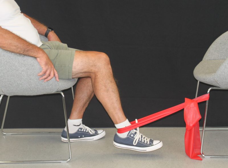 man sat on a chair with one leg stretched out and an exercise band tied to the ankle